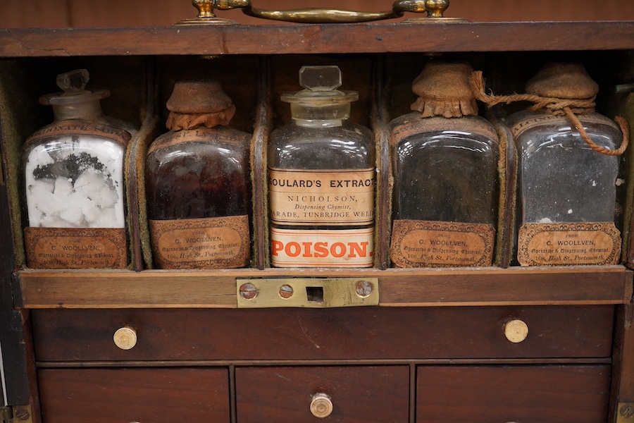 A 19th century mahogany apothecary cabinet, containing 20 bottles of various medicinal compounds and poisons, some sealed, all with paper labels, mainly for ‘C. Woollven, Operative & Dispensing Chemist, 108, High Street,